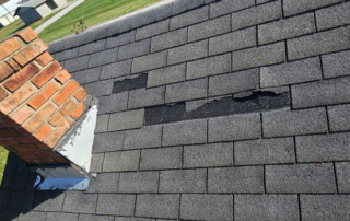 Real-world example of wind-damaged missing asphalt shingles near a brick chimney on a Hamilton County home.