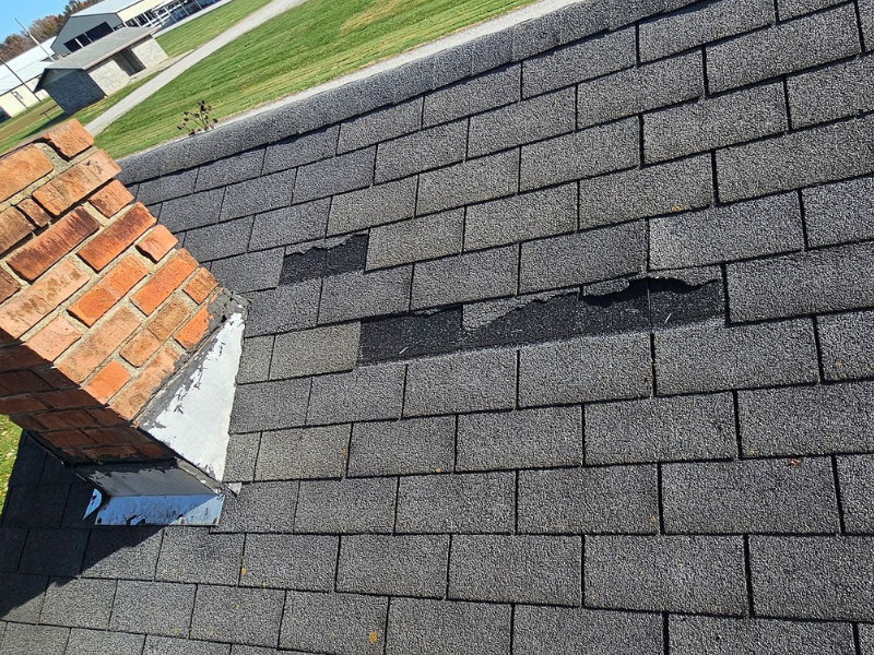 Real-world example of wind-damaged missing asphalt shingles near a brick chimney on a Hamilton County home.